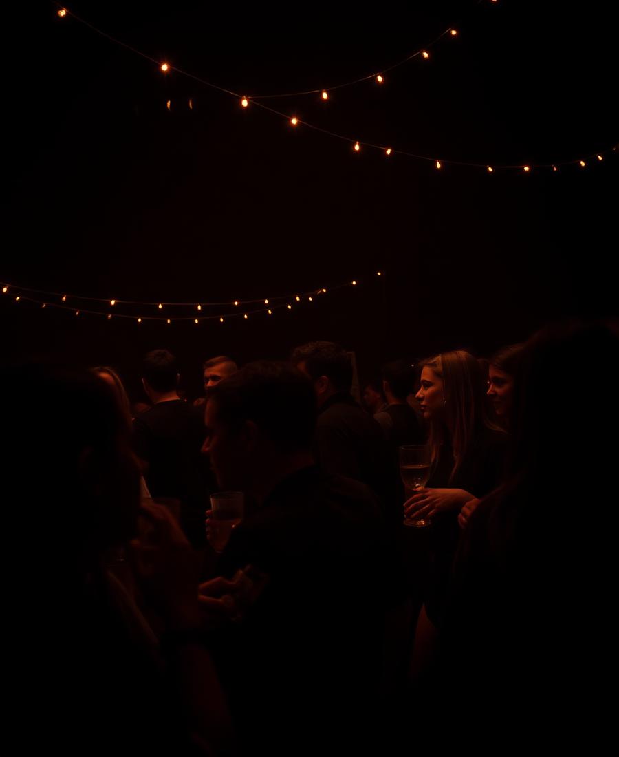 Students socialising with drinks under warm string lights at an evening event
